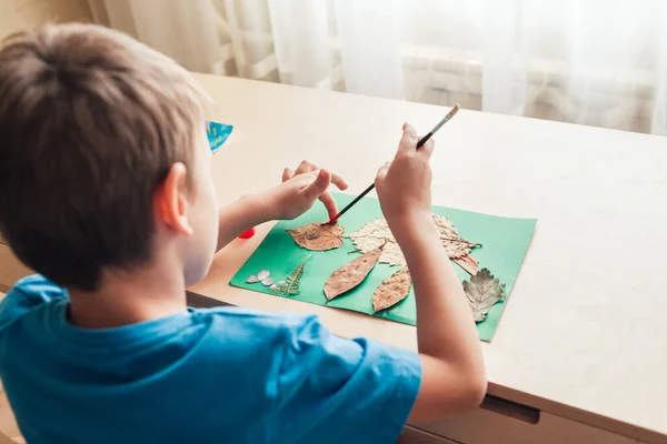 Bambino incolla un applique fatto di foglie autunnali — Foto Stock