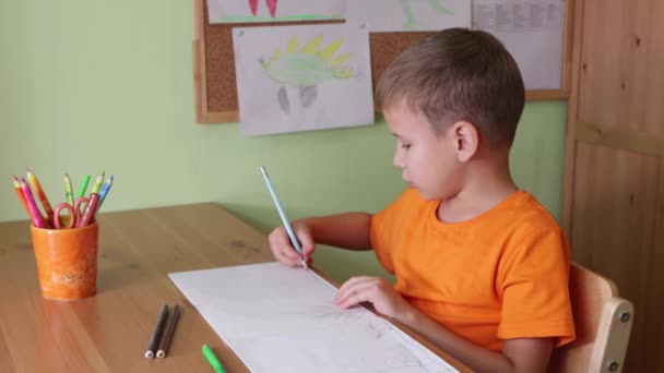 Chico dibujando dinosaurios sentado por escritorio — Vídeos de Stock