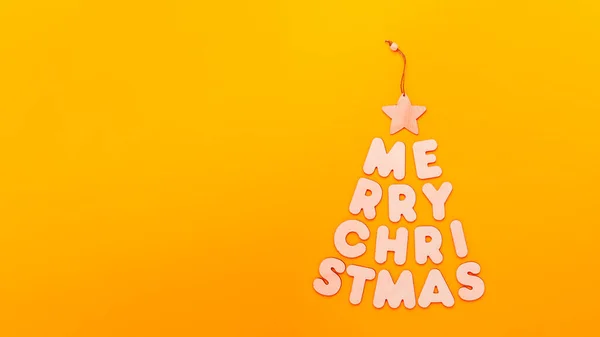 Teks Merry Christmas dalam bentuk pohon cemara pada latar belakang oranye — Stok Foto