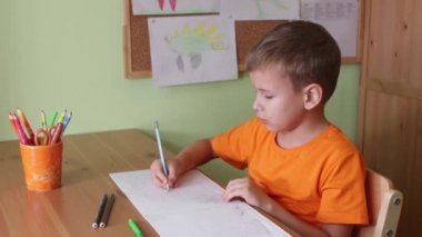 Çocuk masanın başında oturmuş dinozor çiziyor.