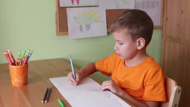 Chico dibujando dinosaurios sentado por escritorio — Vídeo de stock