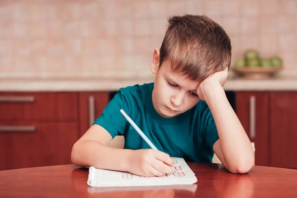 7 Jahre alter Junge sitzt am Tisch in der Küche und schreibt Notizen auf Laken — Stockfoto