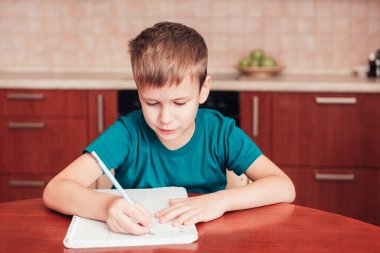 Not defterine mektup yazan sevimli bir çocuk. Masanın başında oturuyor.