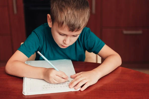 Niño de 7 años escribiendo cartas en cuaderno sentado junto a la mesa — Foto de Stock