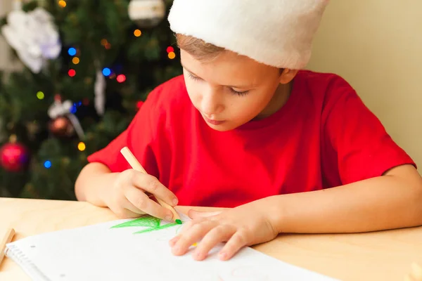 Schattig kind jongen schrijven brief aan de kerstman, kerstboom op de achtergrond — Stockfoto