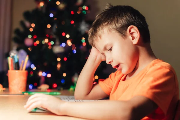 7 Jahre alter Junge sitzt am Schreibtisch und liest Buch — Stockfoto