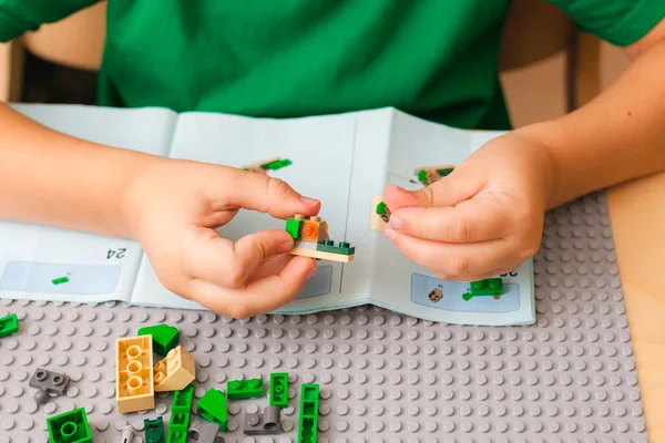 Handen van het kind dat de geleider opvangt Lego volgens instructies — Stockfoto