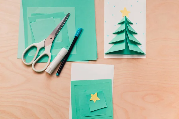 Karácsonyi üdvözlőlap, egy halom színes papír, olló és ragasztó. A gyerek képeslapot készít papírból. 1. lépés — Stock Fotó
