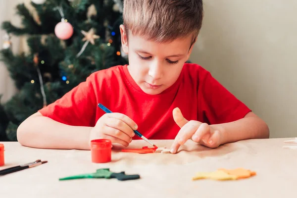 Jongen schildert houten dinosaurus speelgoed voor kerstboom — Stockfoto