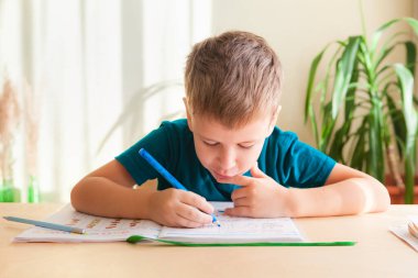 7 yaşındaki çocuk masada oturmuş matematik çalışıyor.
