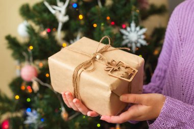 Arka planda süslü Noel ağacı olan kadınların elleri güzel hediyeler tutuyor.