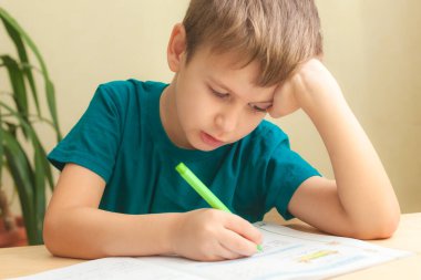 7 yaşında yaşlı bir çocuk masada oturuyor ve ödevlerini yapıyor.