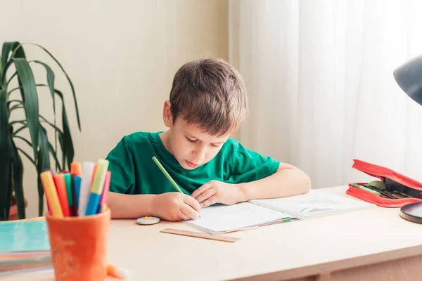 Cute 7 tahun anak melakukan pekerjaan rumahnya duduk di meja — Stok Foto