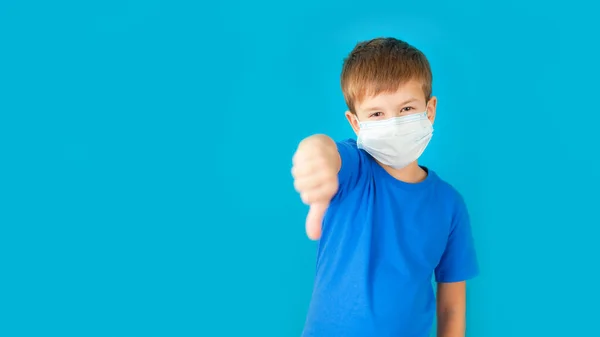 Anak manis dengan masker medis di wajahnya menunjukkan tangan dengan jempol ke bawah — Stok Foto