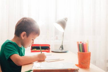 7 yaşında sevimli bir çocuk ödevini yapıyor. Masasında oturuyor.