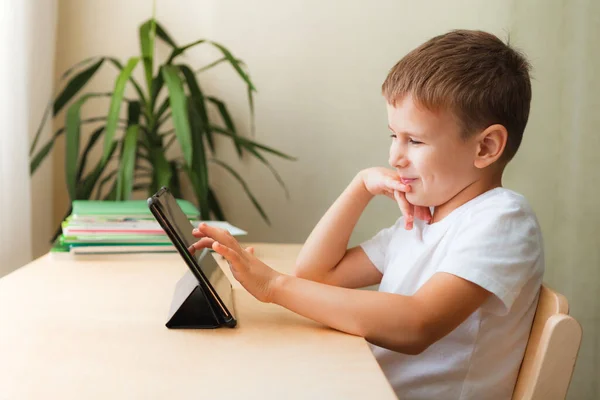 Anak manis duduk dengan tablet di meja. Anak menggunakan gadget untuk belajar dan bermain. — Stok Foto