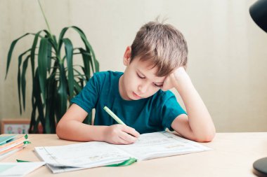 7 yaşında yaşlı bir çocuk masada oturuyor ve ödevlerini yapıyor.