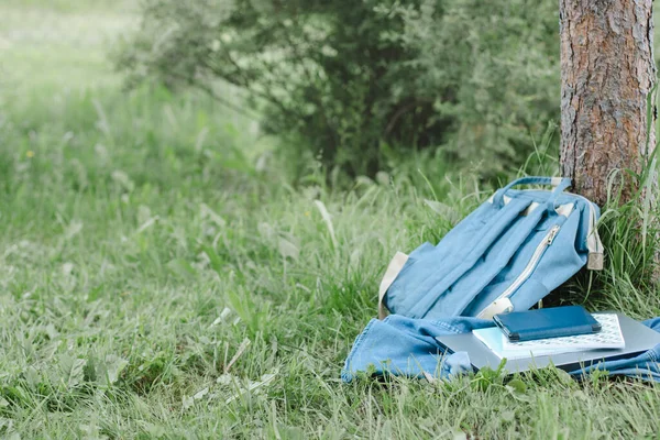 Školní batoh, laptop, zápisník ležící v parku u stromu — Stock fotografie