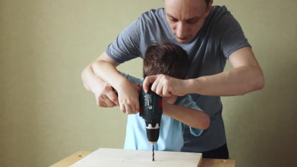 Папа учит сына работать с дрелью, стоя на рабочем месте — стоковое видео
