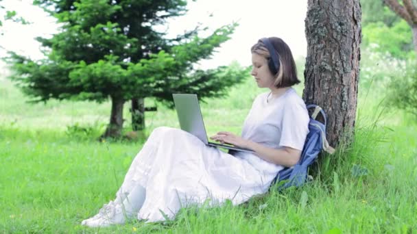 Κορίτσι εκτυπώσεις φοιτητής σε ένα φορητό υπολογιστή, ενώ κάθεται στο πάρκο. Teenager εκτελεί εργασίες σε εξωτερικούς χώρους. — Αρχείο Βίντεο