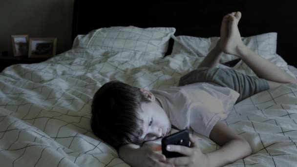 親のベッドに寝そべってスマホを使う少年 — ストック動画
