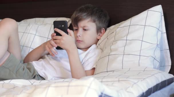 男孩躺在床上用智能手机 — 图库视频影像