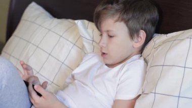 Tatlı çocuk yatakta uzanıyor ve cep telefonuyla oynuyor.