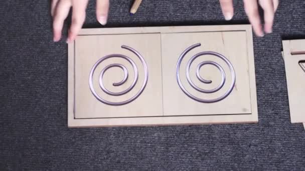 Handen van het kind nemen van sjabloon in de vorm van ronde doolhof en vel wit papier met contouren van dit doolhof erop getekend — Stockvideo