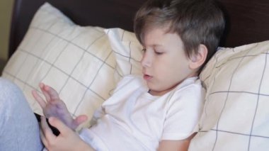 Küçük çocuk yatakta oturuyor ve akıllı telefon kullanıyor.