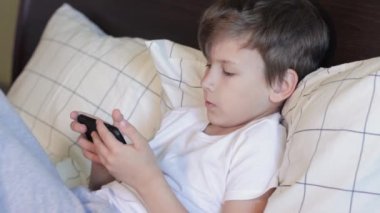 7 yaşında bir çocuk yatakta yatarken alet kullanıyor.