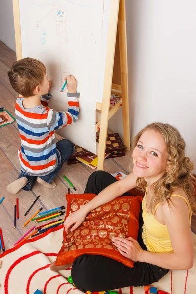 描画彼女の息子と子供部屋に座っている若い女性 — ストック写真