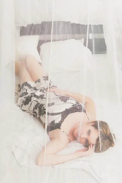 Mujer bonita descansando en la cama detrás de textil transparente —  Fotos de Stock