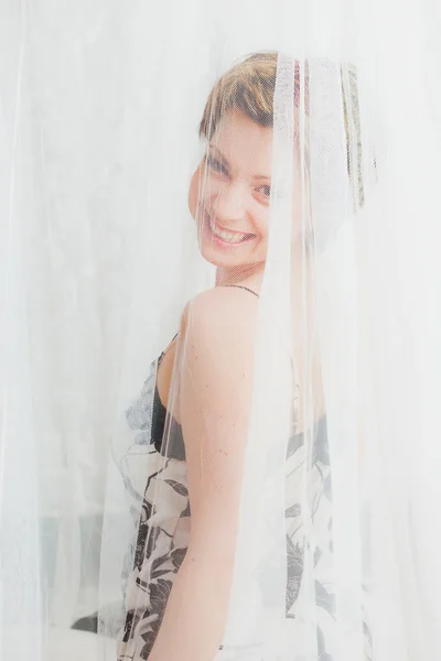 Lächelnde Frau hinter weißem transparentem Textil — Stockfoto