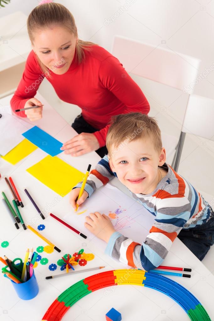 Smiling boy drawing picture with his mother 