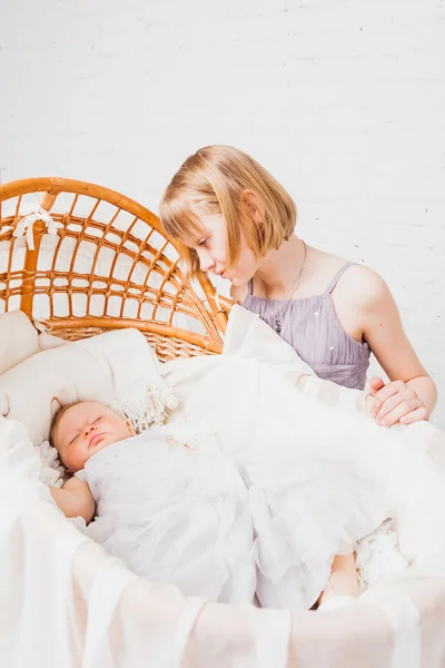 Schönes Mädchen sitzt in der Nähe Wiege mit schlafendem Baby Stockbild