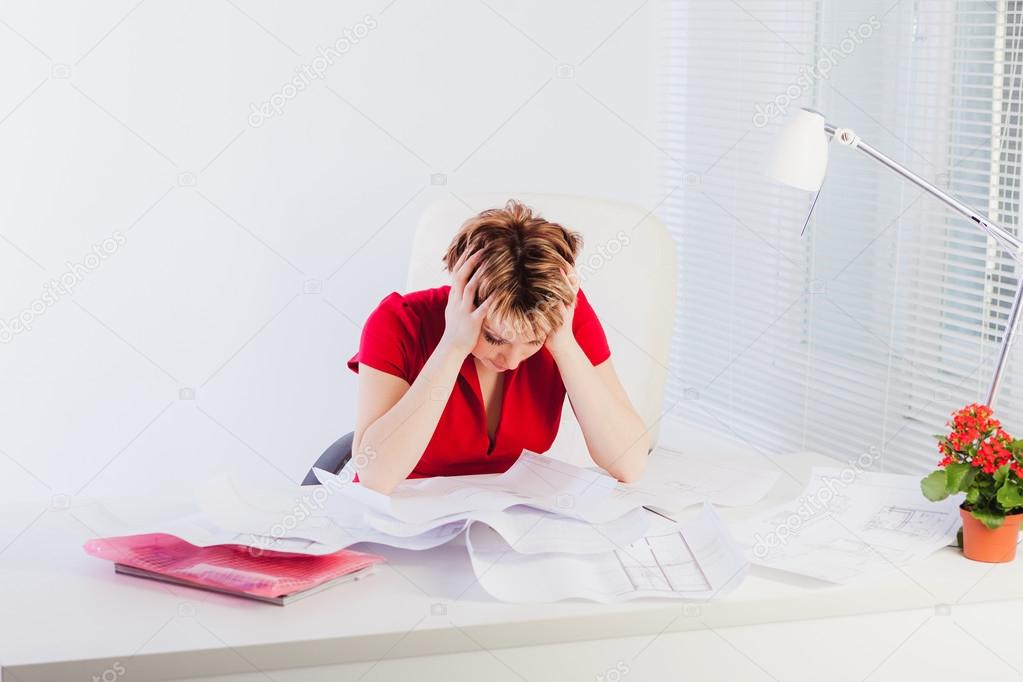 Tired woman holding her head and looking at documents