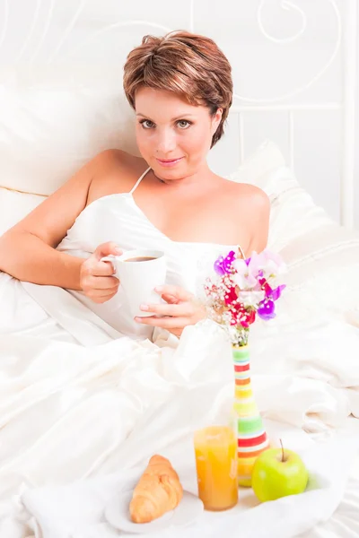 Bella donna beve caffè mentre si siede a letto — Foto Stock