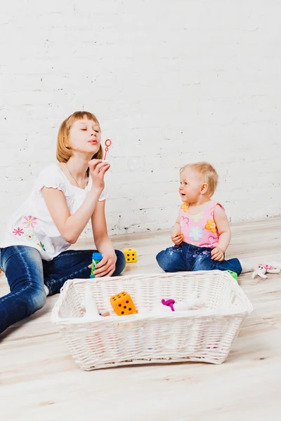 Nice girl blowing bubbles to her little sister — Stock Photo, Image