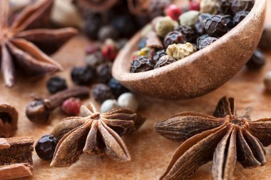 Tahta bir kaşıkta farklı biberlerin tohumları, anason yıldızları, tarçın çubukları ve ahşap bir masada karanfiller. Seçici odaklanma. Makro.