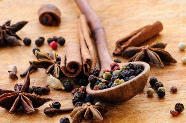 Tahta bir kaşıkta farklı biberlerin tohumları, anason yıldızları, tarçın çubukları ve ahşap bir masada karanfiller. Seçici odaklanma. Makro.