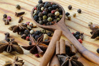 Tahta bir kaşıkta farklı biberlerin tohumları, anason yıldızları, tarçın çubukları ve ahşap bir masada karanfiller. Seçici odaklanma. Makro.