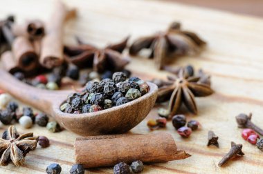 Tahta bir kaşıkta farklı biberlerin tohumları, anason yıldızları, tarçın çubukları ve ahşap bir masada karanfiller. Seçici odaklanma. Makro.