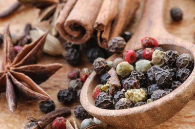 Tahta bir kaşıkta farklı biberlerin tohumları, anason yıldızları, tarçın çubukları ve ahşap bir masada karanfiller. Seçici odaklanma. Makro.