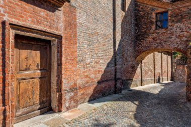 Guarene, Piedmont, Kuzey İtalya 'da dar bir kaldırım taşı caddesindeki eski evin ahşap kapısı ve tuğla duvarı..