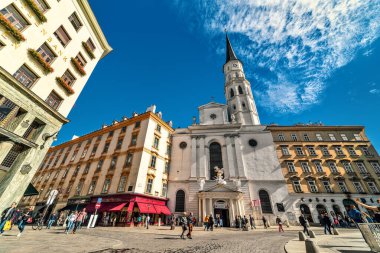 VIENNA, AUSTRIA - SEPTEMBER 27, 2018: View of St Michaels Church under blue sky and people walking on the street in old historic part of Vienna - capital city, famous and popular tourist destination.