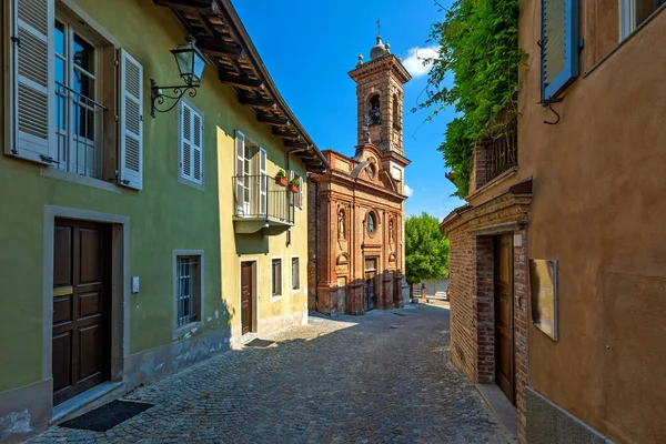 意大利北部皮埃蒙特 蓝色天空下的房屋和古老的砖瓦教堂之间狭窄的鹅卵石街 — 图库照片