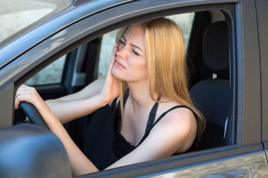 Sarışın kadın araba kullanırken diş ağrısı çekiyor.