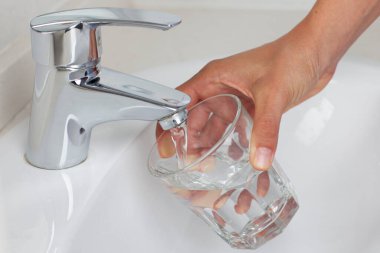 Kadın musluktan bardağa su dolduruyor.