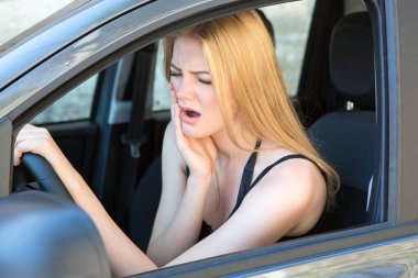Genç bir kadın araba kullanırken acı çekiyor. 
