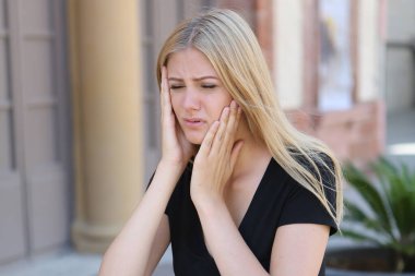 Sarışın kadın dışarıda otururken diş ağrısı çekiyor.